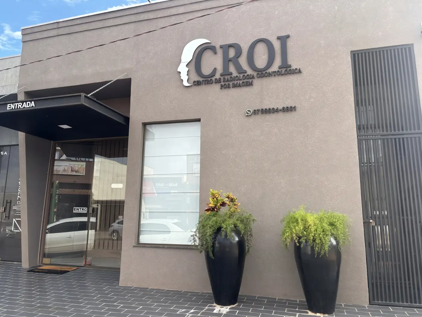 Fachada da CROI em Ivinhema, com o letreiro na parede, a entrada coberta e dois vasos de plantas